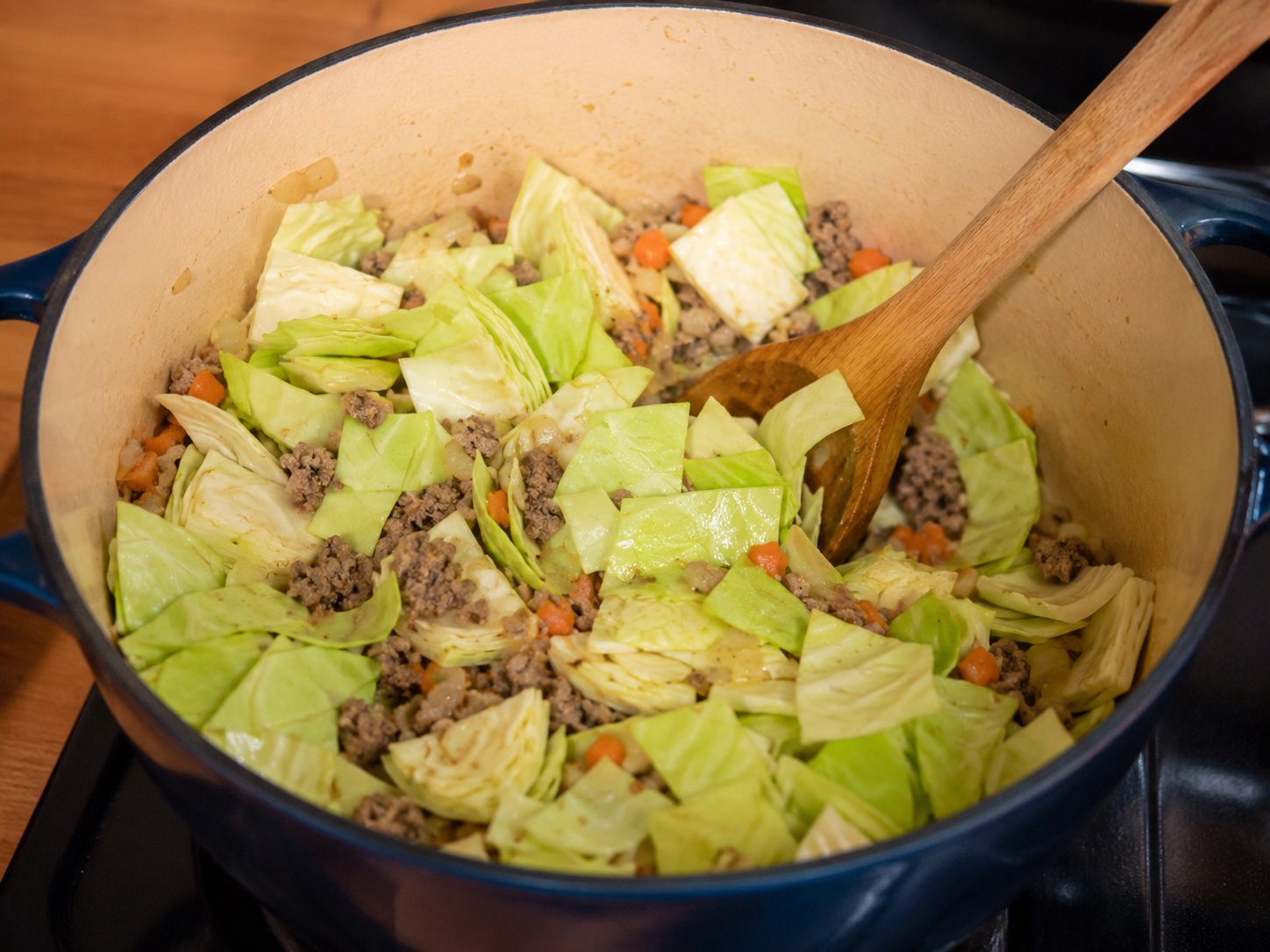 Chopped cabbage stirred into a pot with ground beef, onion, garlic, and carrot.
