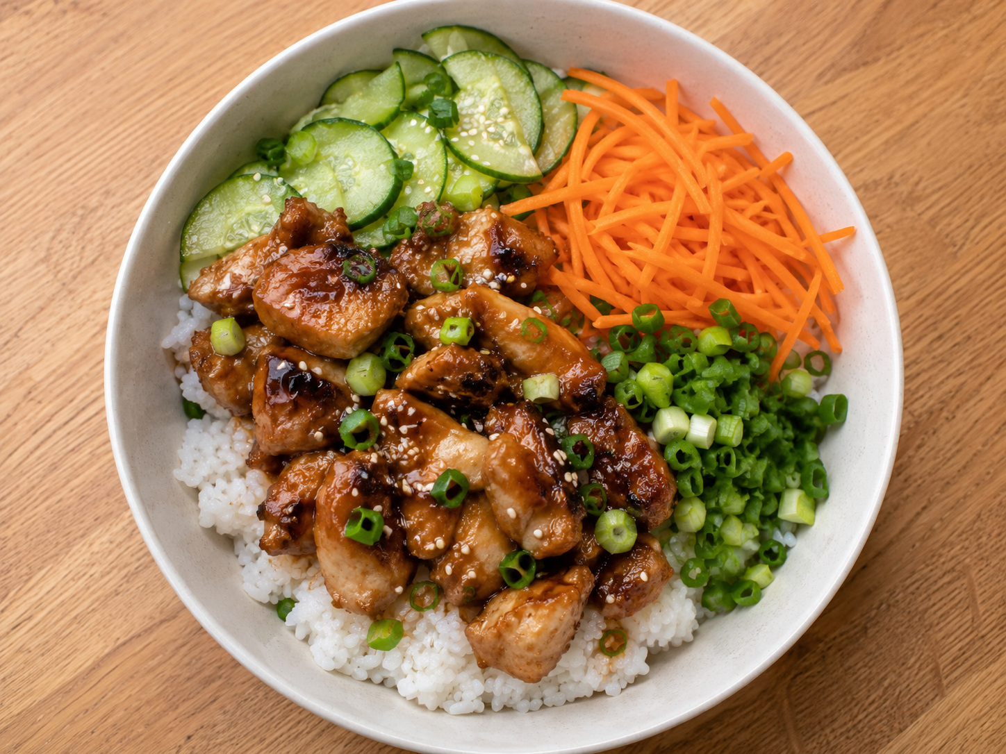 Teriyaki chicken rice bowl with saucy chicken, white rice, cucumber, carrots, green onions, and sesame seeds.