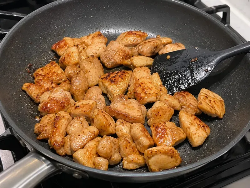Chicken pieces cooking in a skillet until golden for teriyaki chicken rice bowls.
