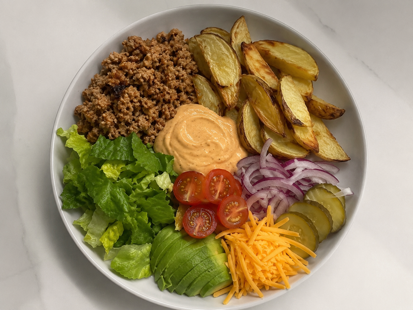 Turkey burger protein bowl with ground turkey, roasted potatoes, lettuce, tomatoes, pickles, red onion, and burger sauce.