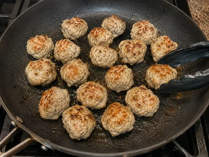 Turkey meatballs browning in a skillet with olive oil.