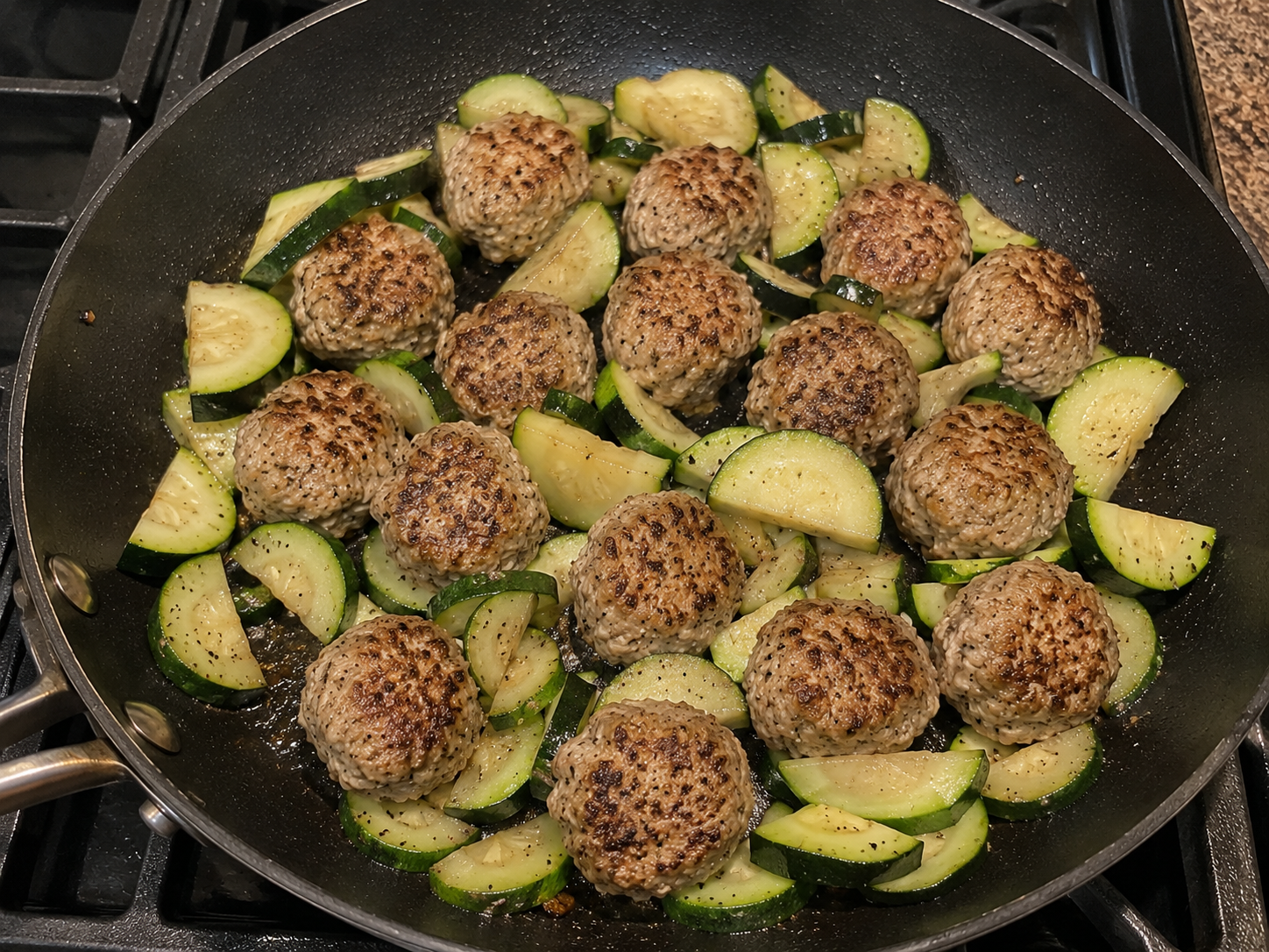 Sliced zucchini added to browned turkey meatballs in a skillet.