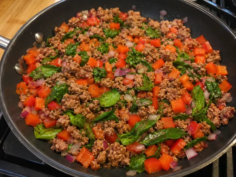 Turkey sausage cooked with bell pepper, red onion, and spinach in a skillet.