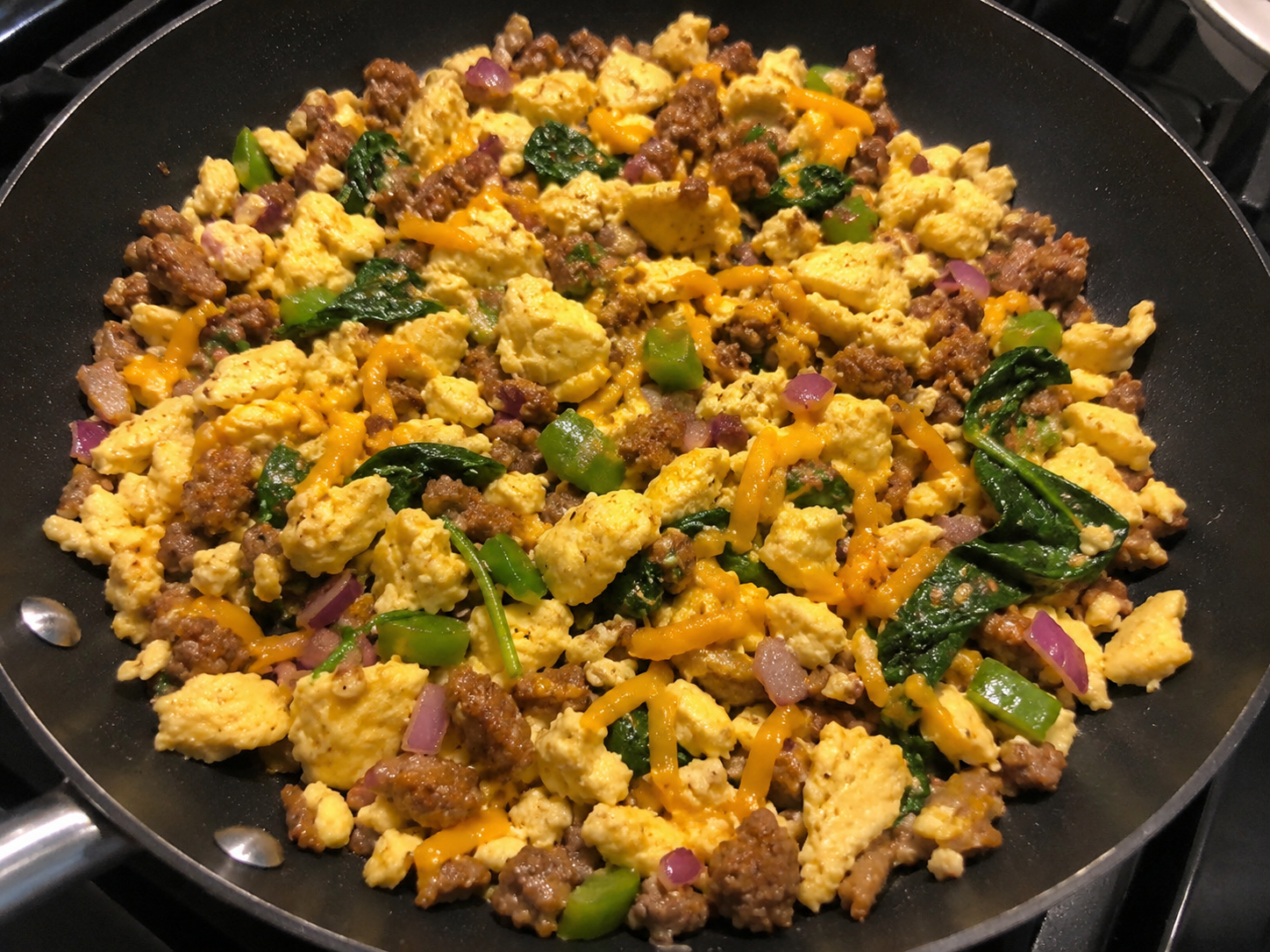 Scrambled eggs cooked with turkey sausage, vegetables, and melted cheddar in a skillet.