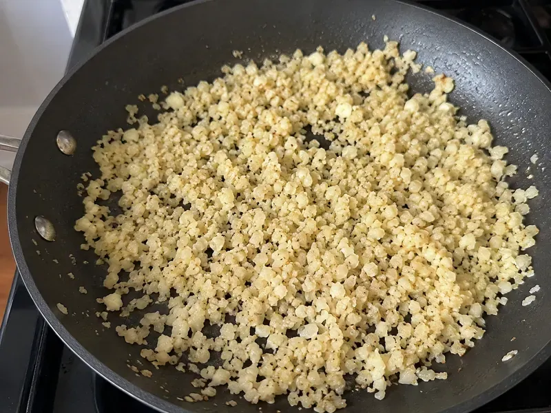Cauliflower rice cooking in a skillet with olive oil and salt.