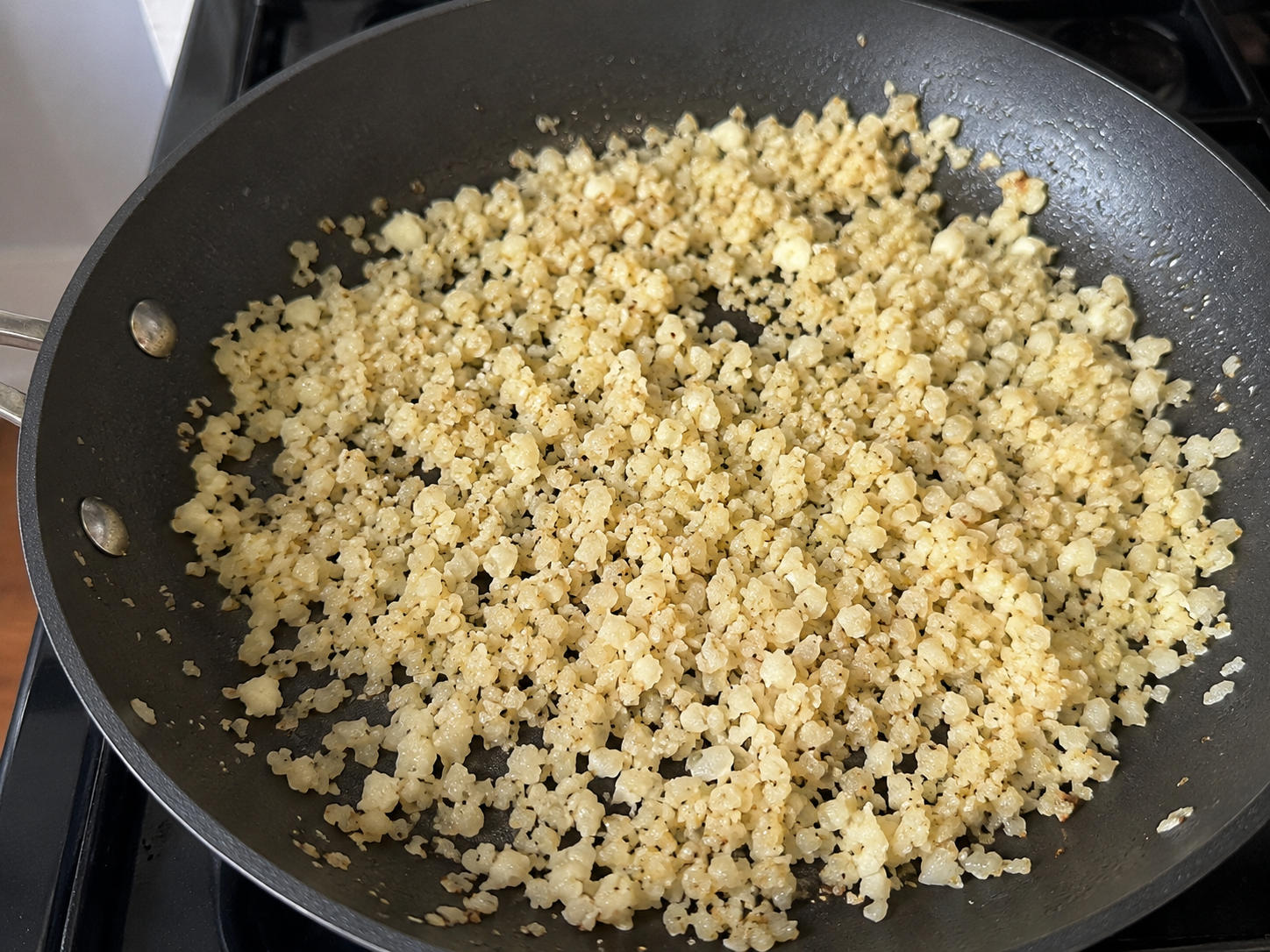 Cauliflower rice cooking in a skillet with olive oil and salt.
