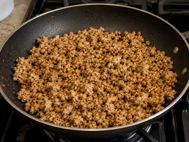 Ground turkey cooking in a skillet with taco seasoning for a turkey taco rice bowl.
