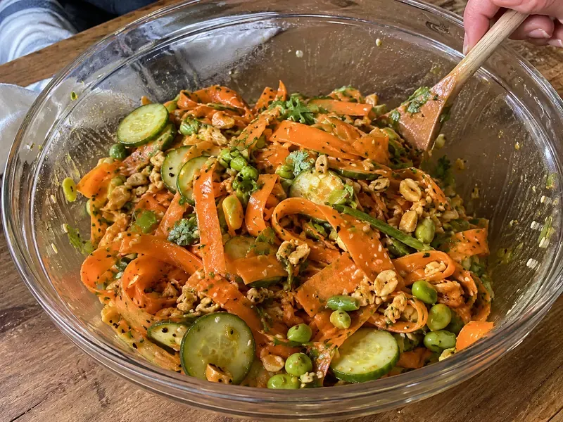 Carrot ribbon salad tossed with cucumber, green onions, peanuts, sesame seeds, edamame, and dressing.